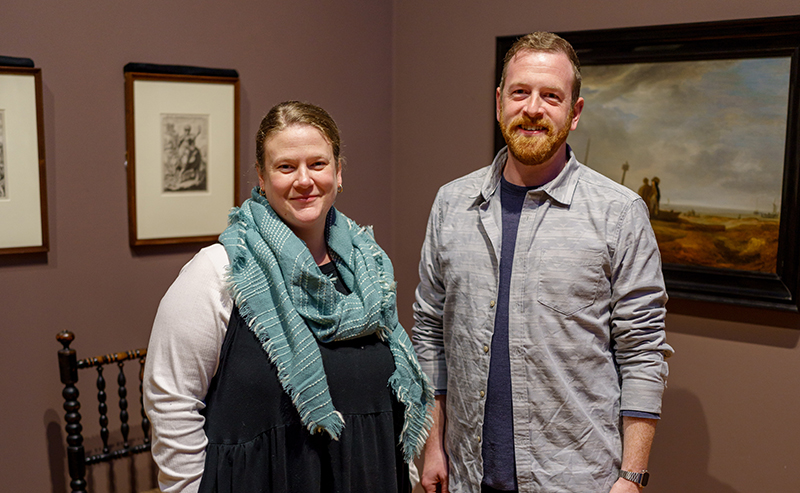A woman with a flowing scarf and a man with a beard standing next to each other in an art gallery