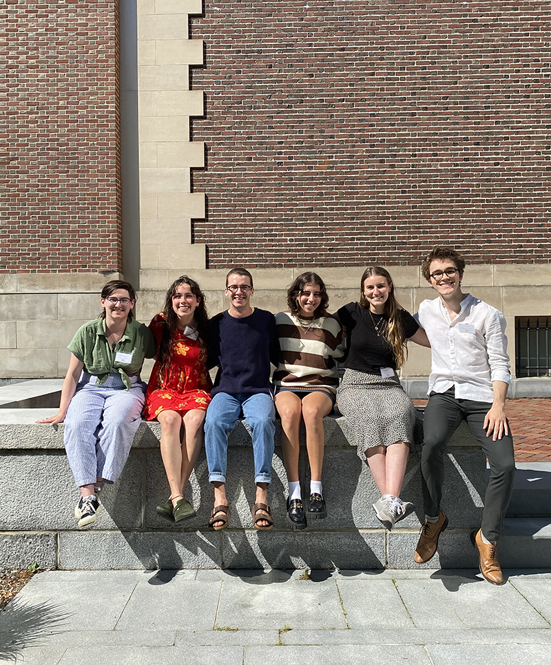 Six young people sitting on a wall in front of a brick building