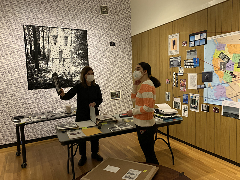 Two women standing in a gallery, with a table and exhibition materials