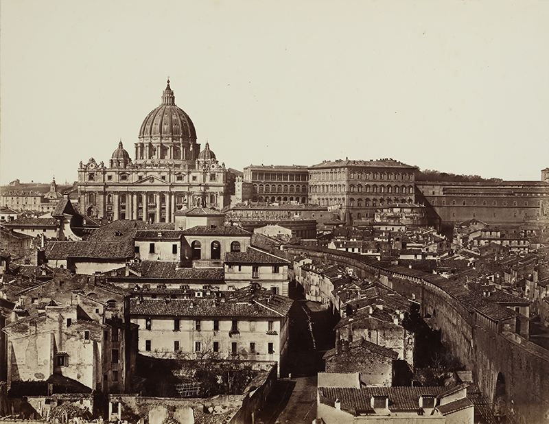 An old, sepia, photograph showing a basilica on a hill, surrounded by other buildings, in Rome