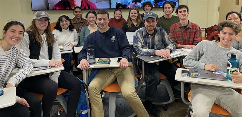 A group of smiling students sitting at classroom desks
