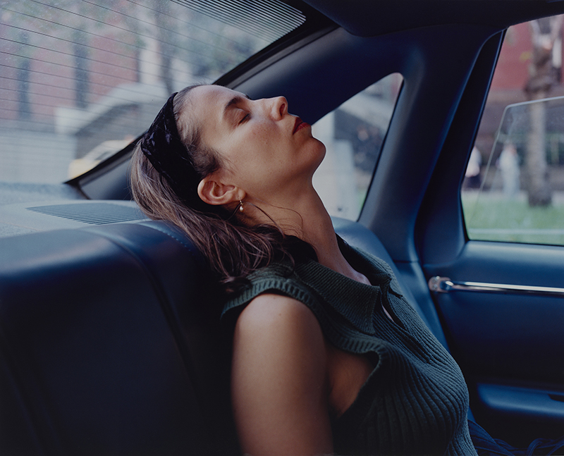 a color photograph showing a woman with long hair leaning back in the seat of a car