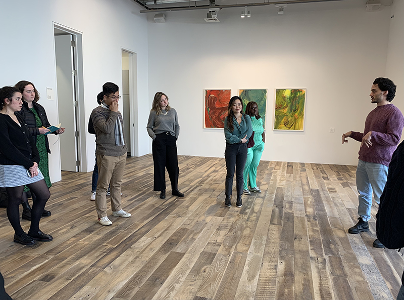 A group of people in an art gallery listening to a speaker