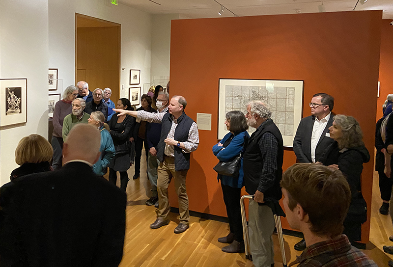 A group of people in a gallery with art on the walls. One gentleman is pointing.