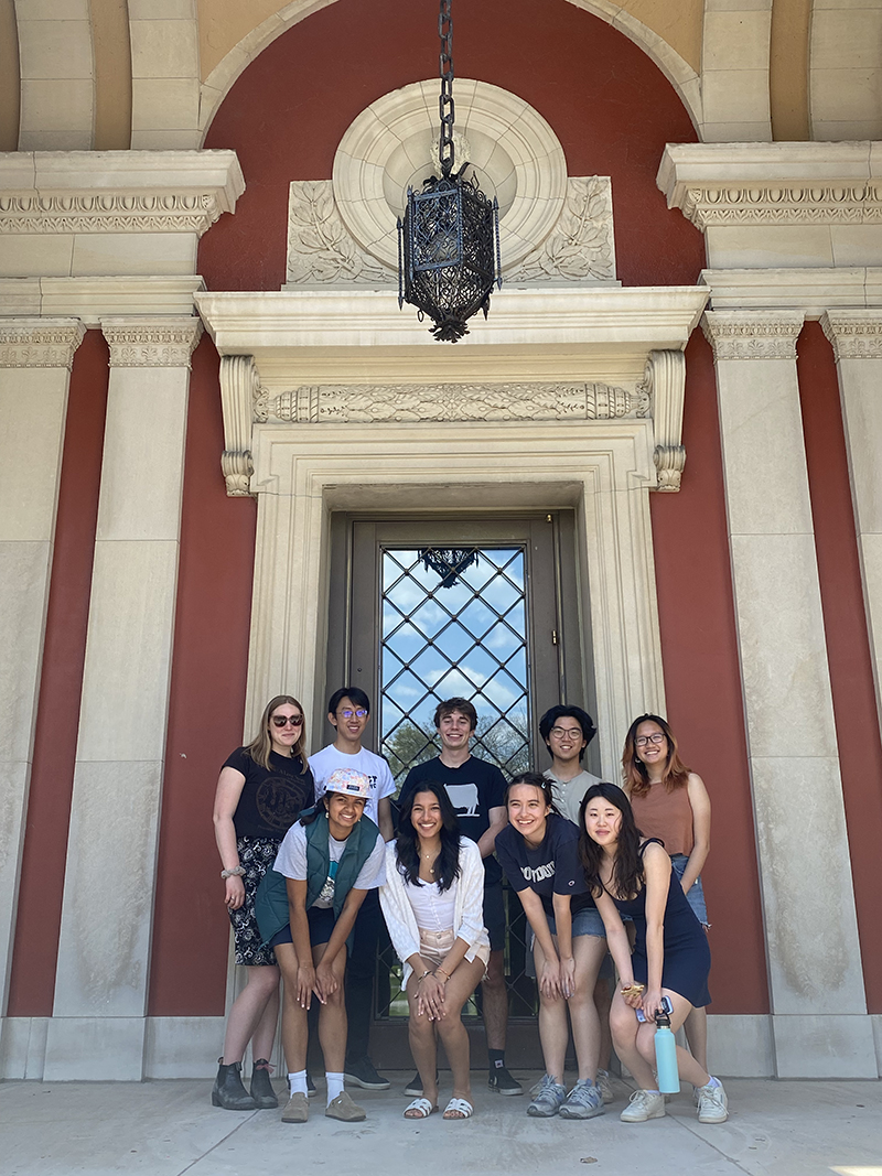 A group of 8 people posing in front of an ornate door