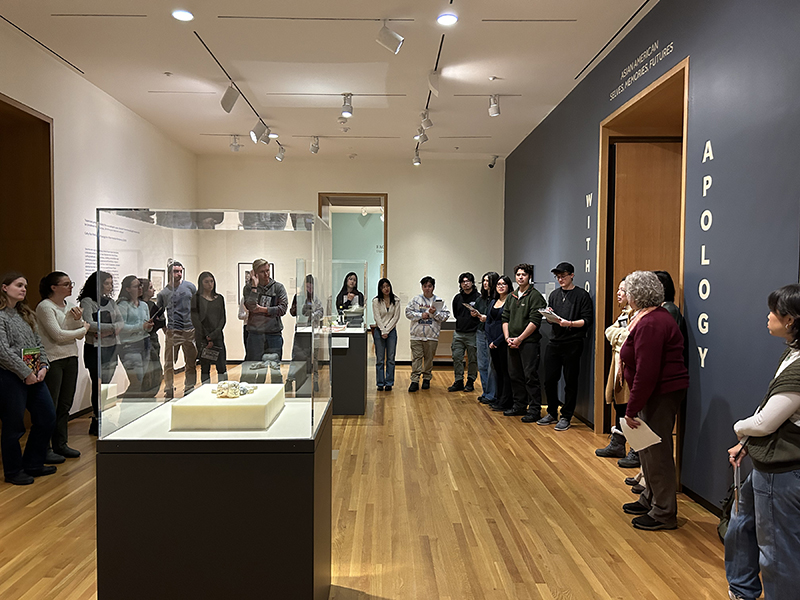 A group of people standing and listening in an art gallery with grey walls