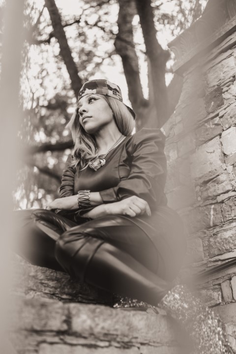 woman sits in profile on a stone wall with arms crossed