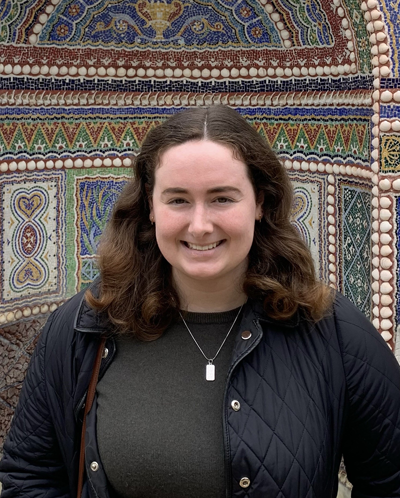A smiling woman standing in front of a mosaic wall
