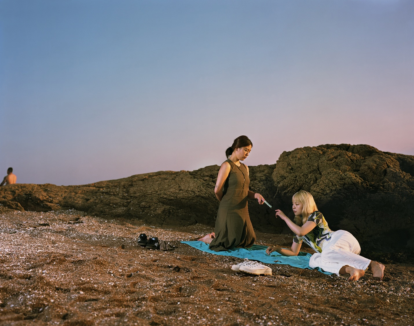An fine art photograph shows two people on a blanket on a sandy beach and one holds a finger trap puzzle game