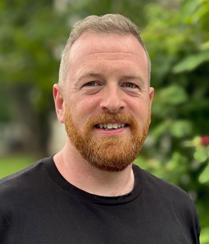 A headshot of a person in a black t-shirt