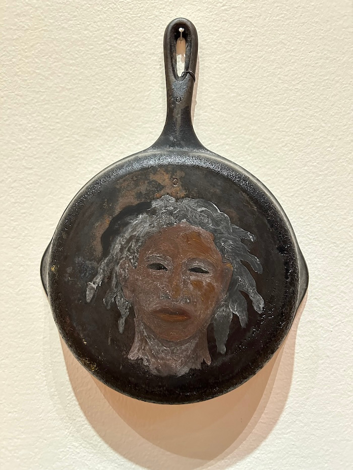A painted portrait of a person with dark skin on a cast iron skillet