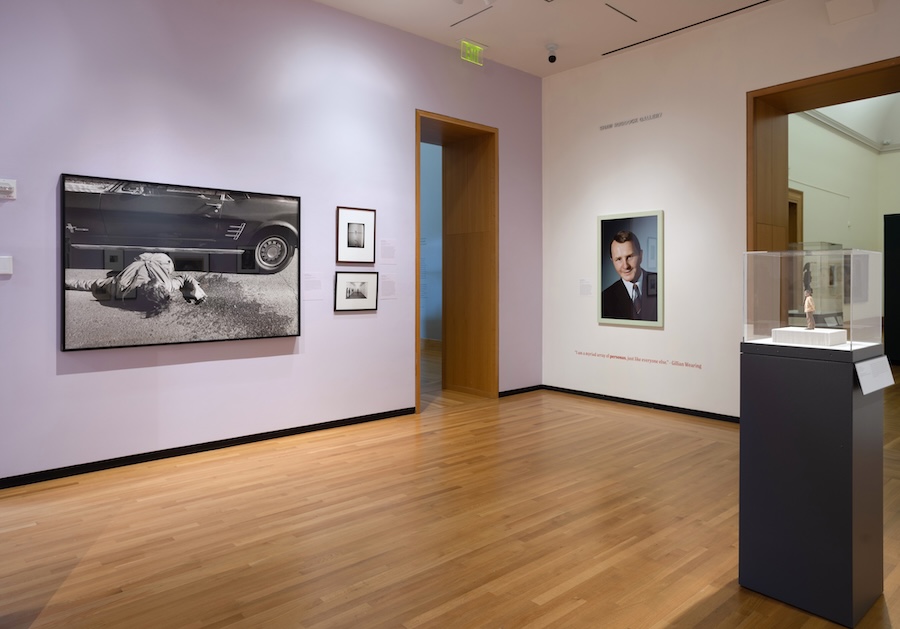 An art museum space with lavender walls displays framed photographs