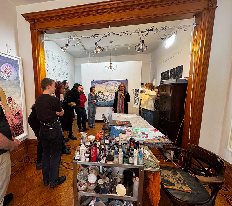 People gather in an artist's studio to look at colorful artwork