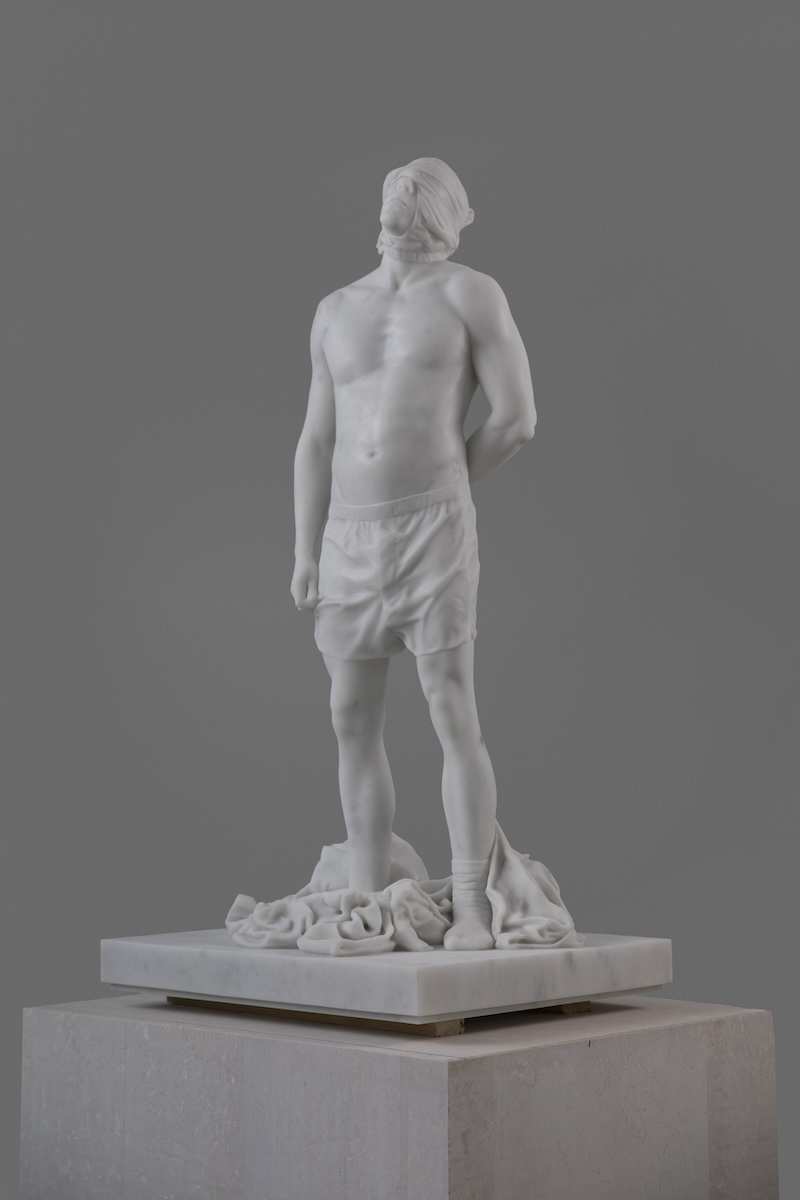 A freestanding marble sculpture shows a disrobed male figure with his eyes obscured