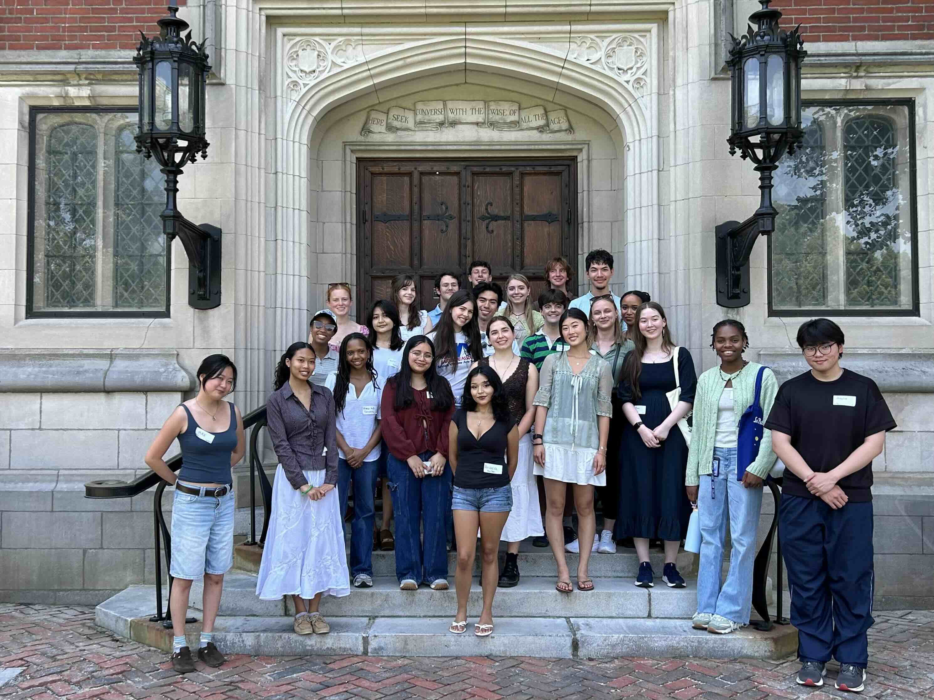 A large group of student interns pose in front of an academic building on a college campus