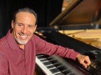 A musician sits next to a piano