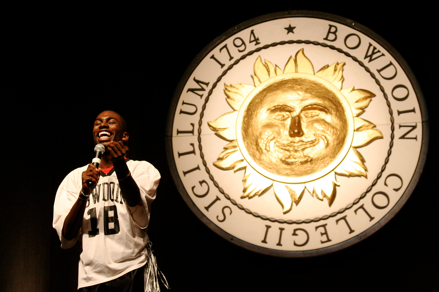 A student performs improv comedy in front of the college seal.