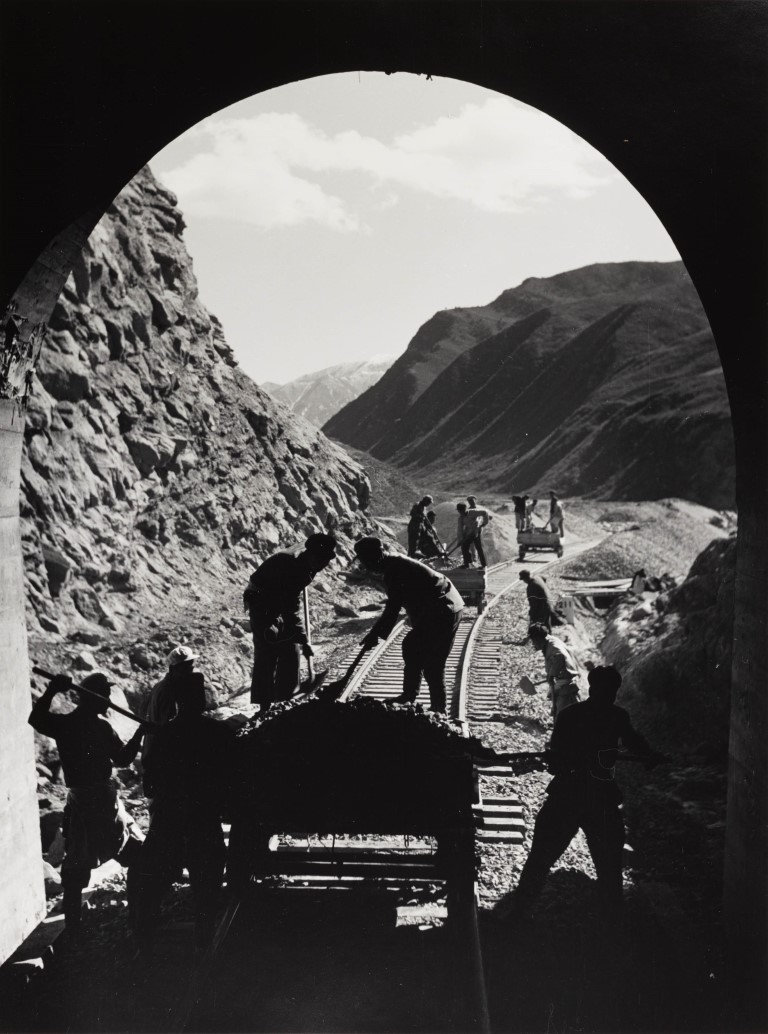 workers toiling on a railway just outside a tunnel in a mountainous landscape