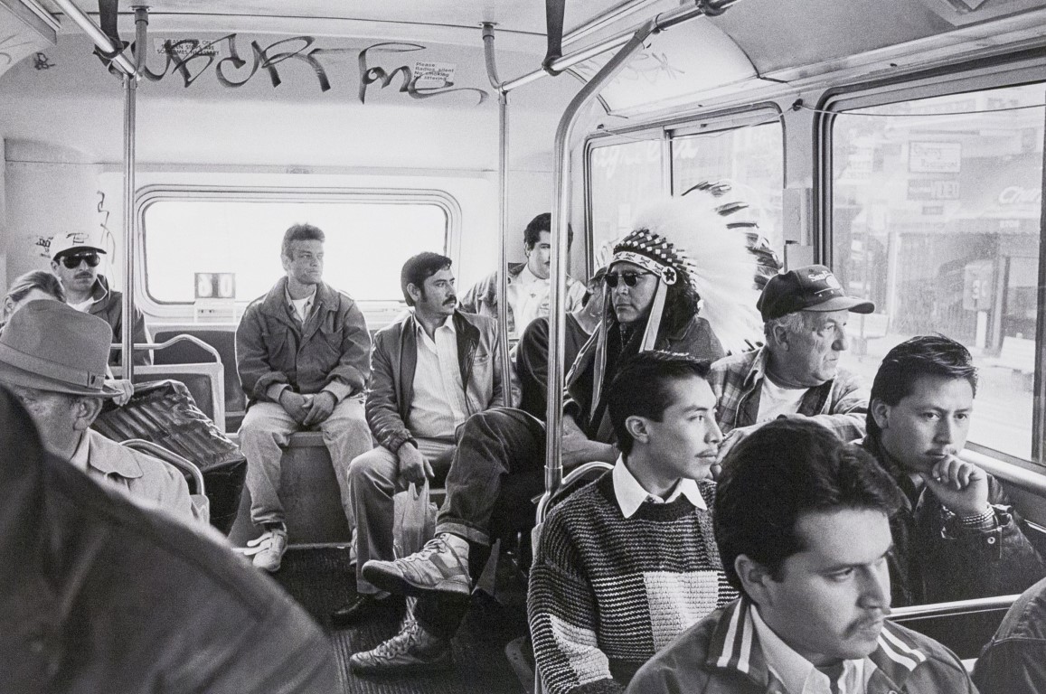several men seated in a bus one of them wearing a feathered headdress