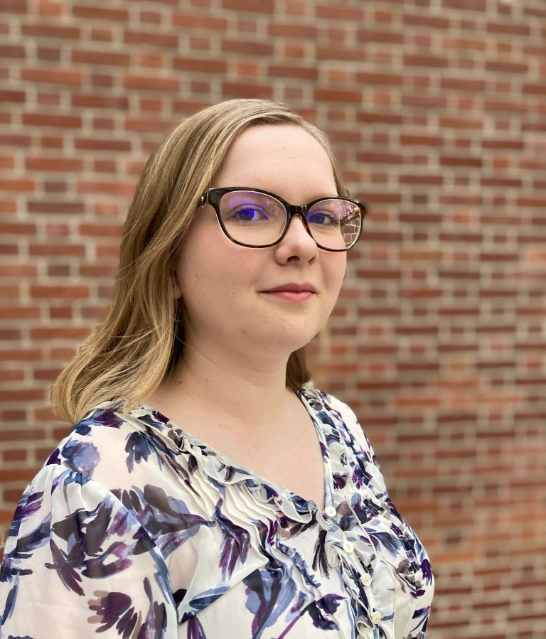 student in glasses and blouse poses in front of brick wall