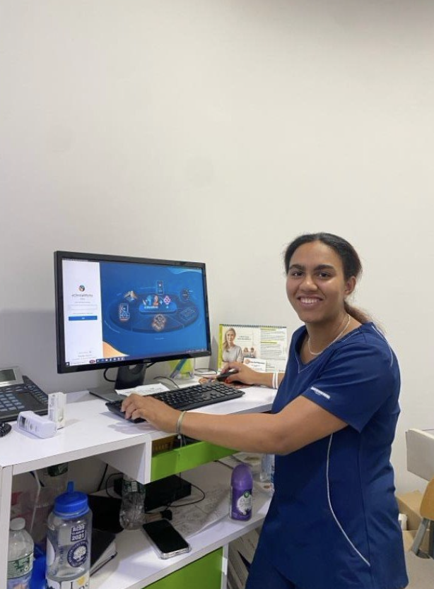 Arly Rodriguez poses next to a computer while donning the medical uniform of their office.