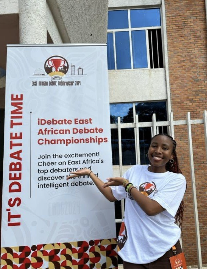 Aurélie stands next to a sign for iDebate's East African Debate Championship.