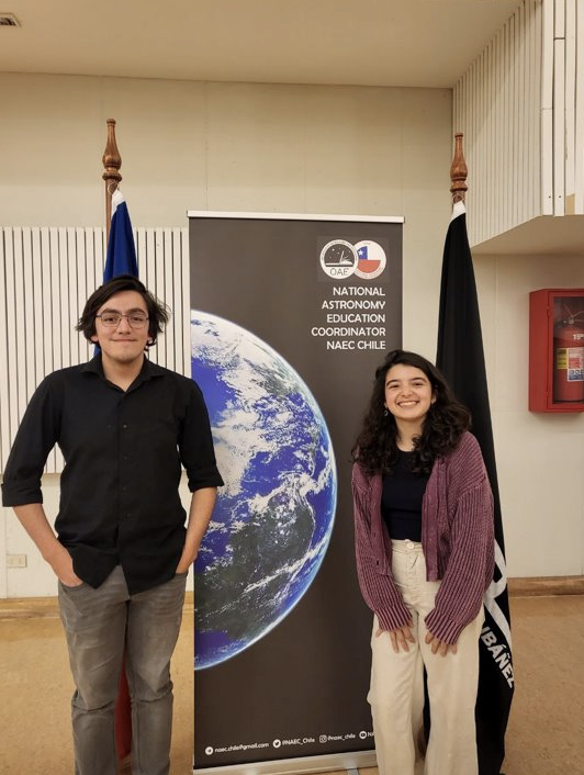 Benjamin poses with a coworker in front of a National  Astronomy Education sign.