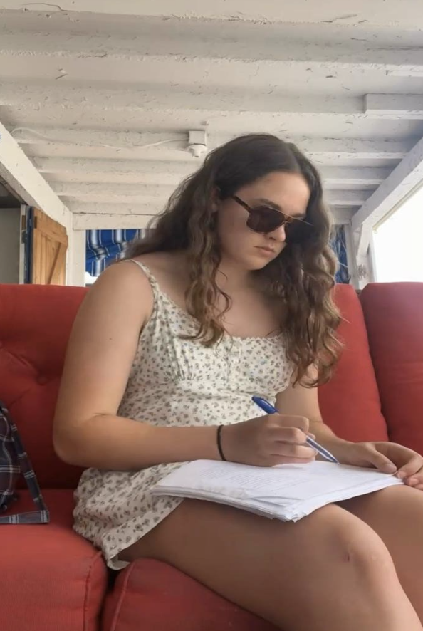Charlotte reads a manuscript while seated on a couch. 