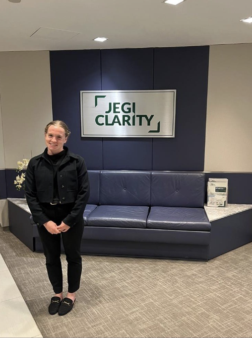 Elizabeth poses in JEGI CLARITY's lobby, next to the sign.