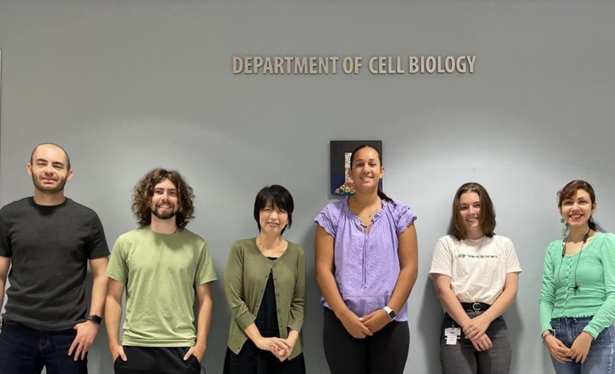Emily poses with their research team in front of the Department of Cellular Biology.