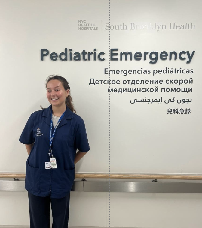 Emma poses next to the Pediatric Emergency sign at South Brooklyn Health hospital.