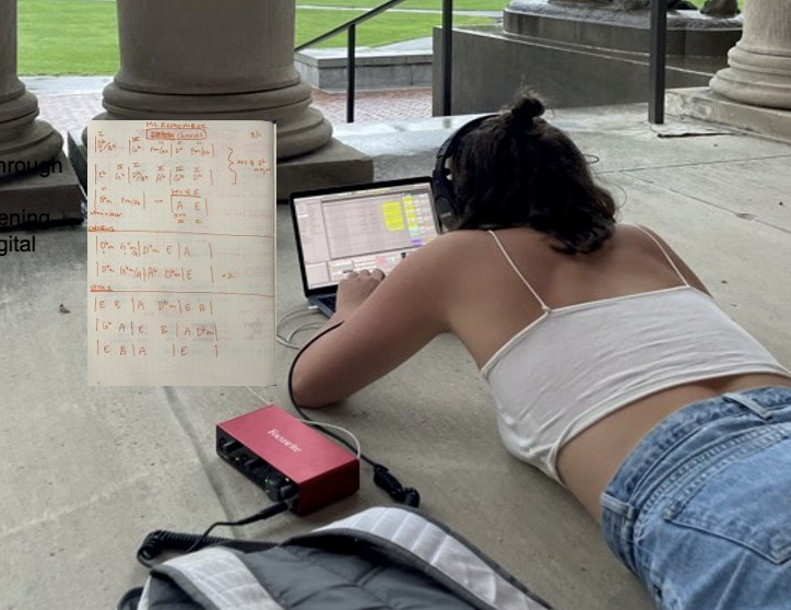 Frances lies on the ground working on music on laptop. 