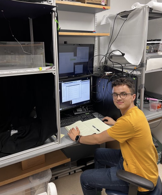 Lionel works at their lab space, jotting down notes from the screen in front of them.