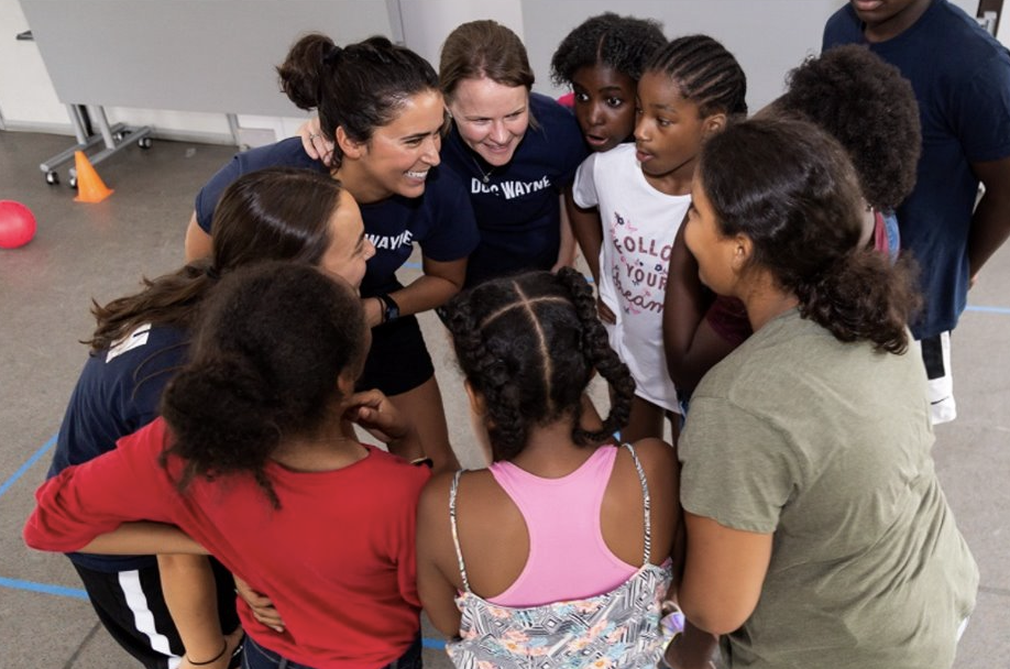 Maya pictured in a group huddle with coworkers and young students.