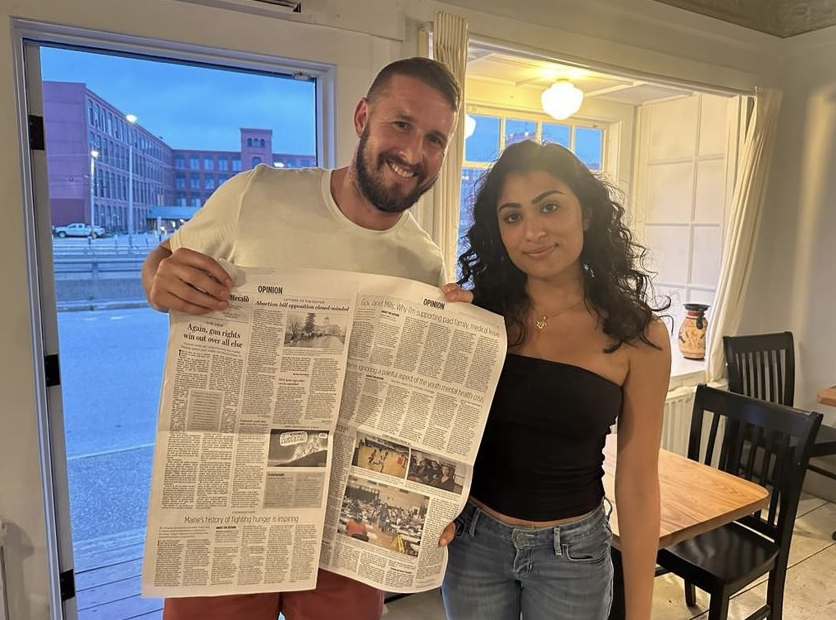 Megh poses with a coworker while holding up the Portland Press Herald​ newspaper.