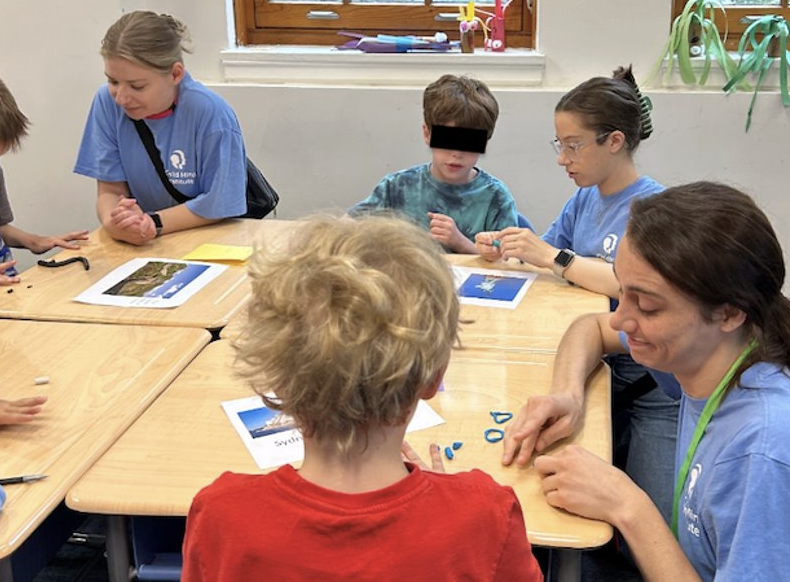 Molly works with children at a table, helping them with a learning activity.