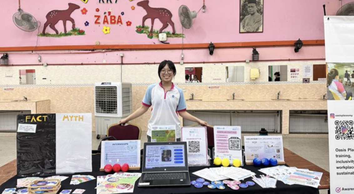 Nat poses in front of a table demonstrating Oasis Place Malaysia's services and work.