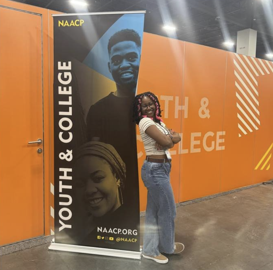 Rachea poses next to sign for the NAACP Youth and College Division​.