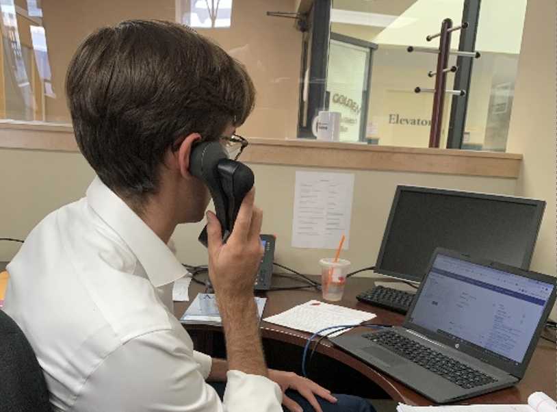 Students sits in front of computer, phone in hand.