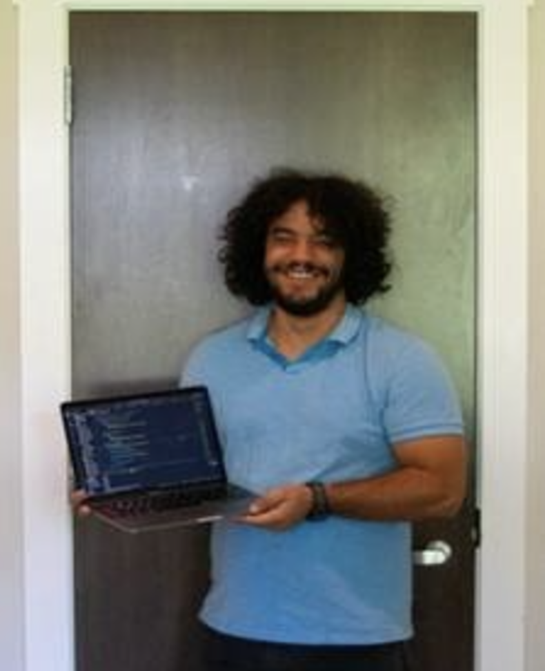 Yassine poses with their laptop showing a script.