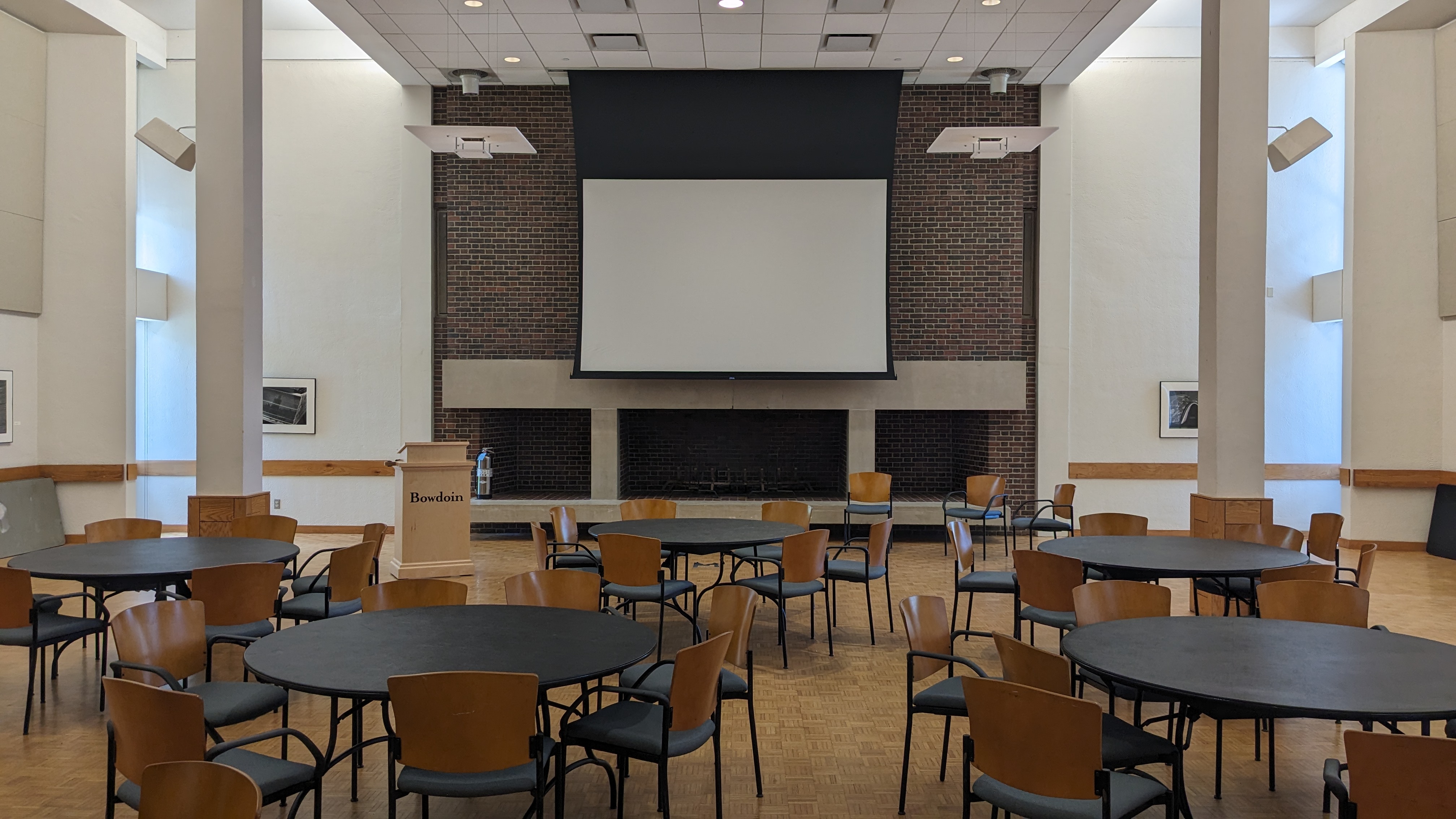 Large stone fireplace, round tables iwth chair in a space with a high ceiling and lots of natural light. 