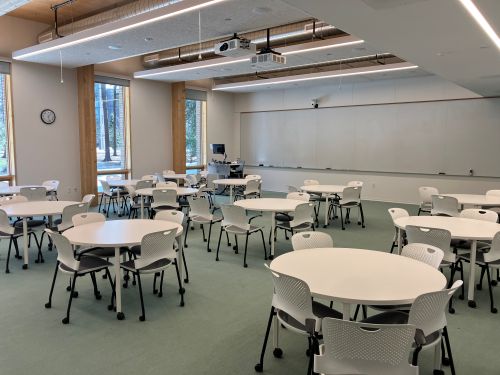 Mills Hall 103 - large classroom with round white tables and green carpet