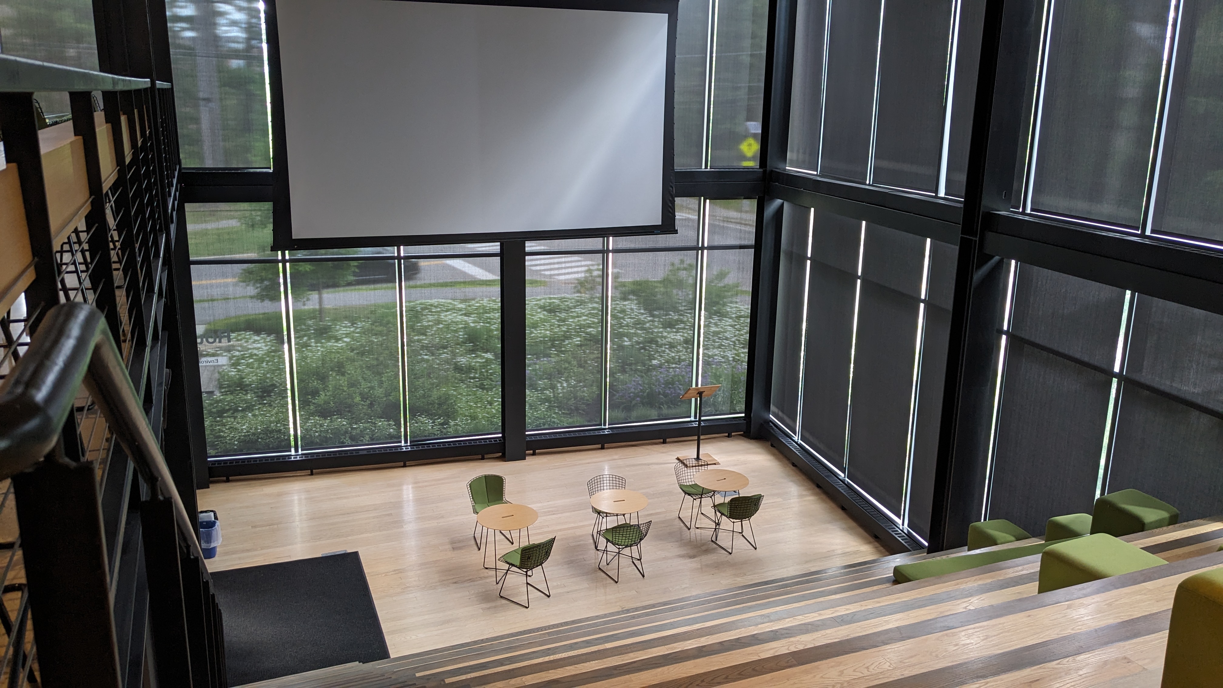 Indoor bleacher seating. The walls are all windows. There are green square cushions on the bleachers. 