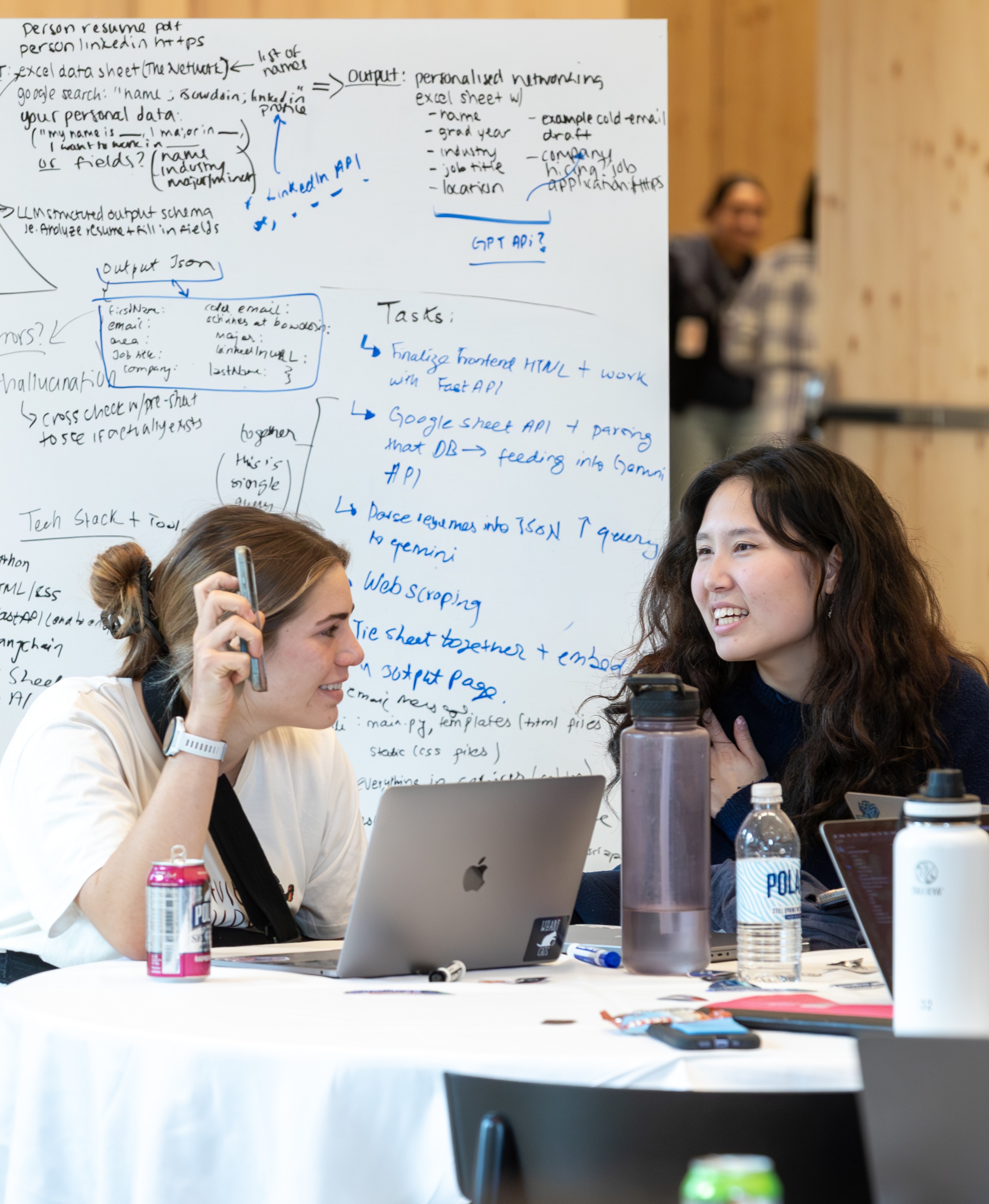 Students collaborating at laptops during the AI Hackathon with a whiteboard in the background
