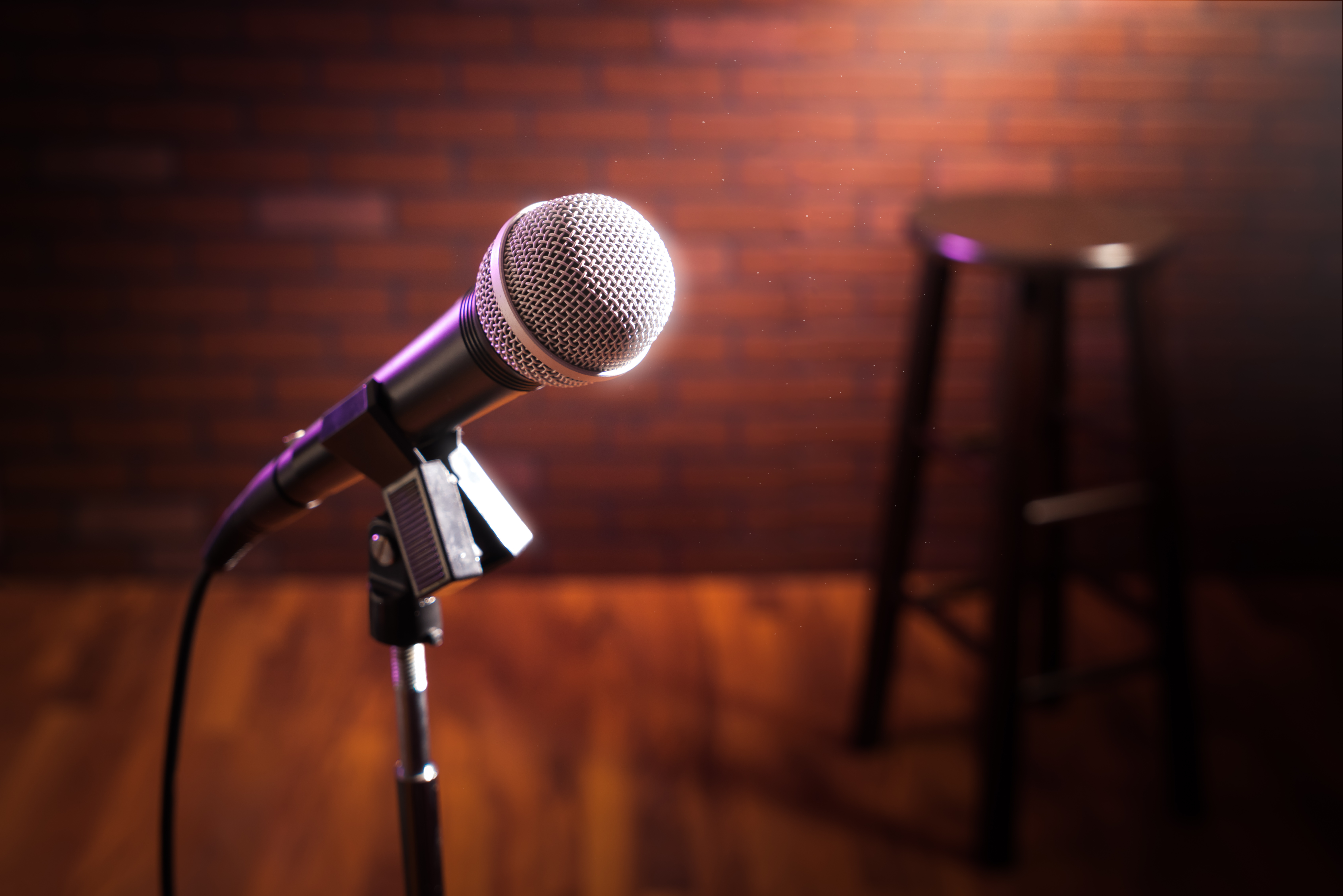 A microphone stand and stool on an empty stage with a brick wall backdrop