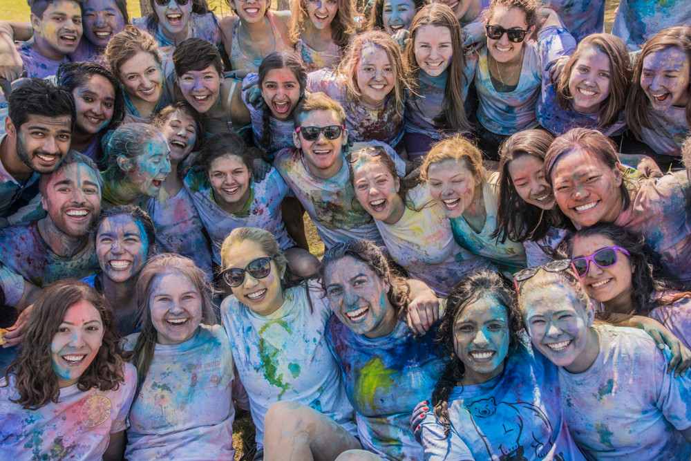 A large group of students affiliated with South Asian Student Association smiles at the camera while covered in dye following their annual Holi celebration
