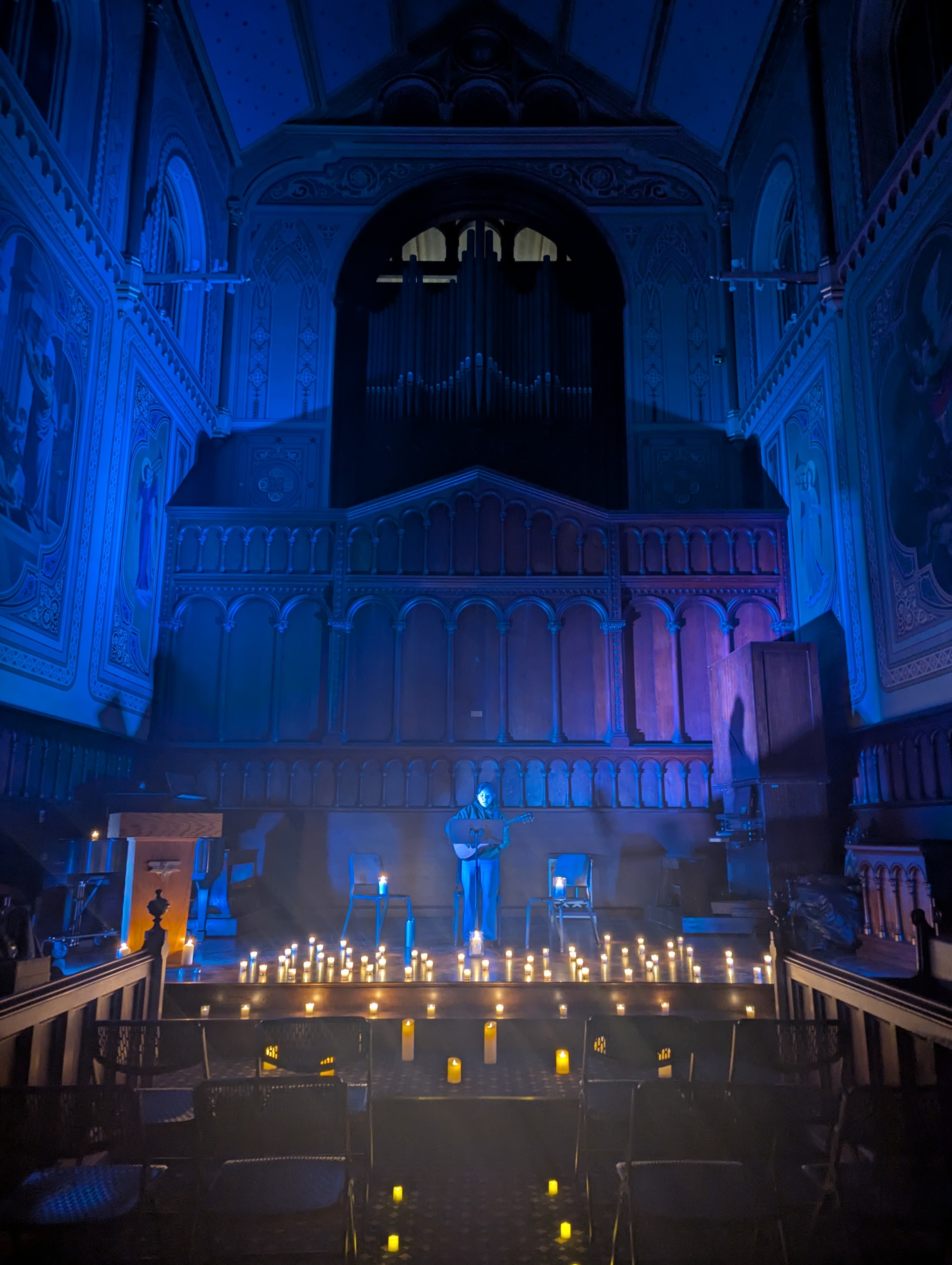 Guitarist Whitney Pelegrino plays reflective acoustic music on the stage of the chapel flanked by candelight and warm, blue lights