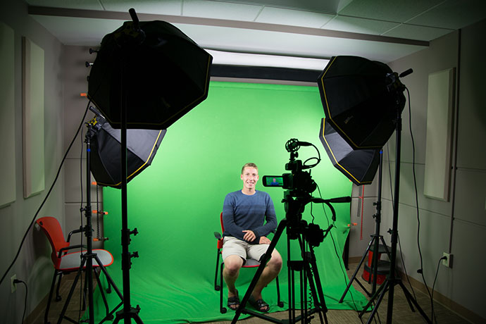 student sits in front of green screen in studio