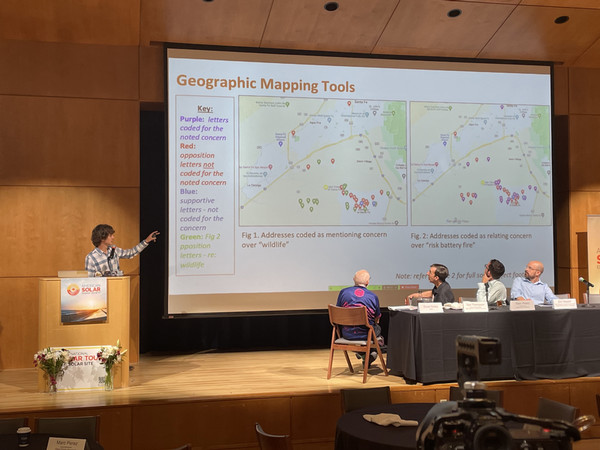 Colter stands at a podium pointing at a projector screen behind him, presenting a slide entitled 'Geographic Mapping Tools'. 