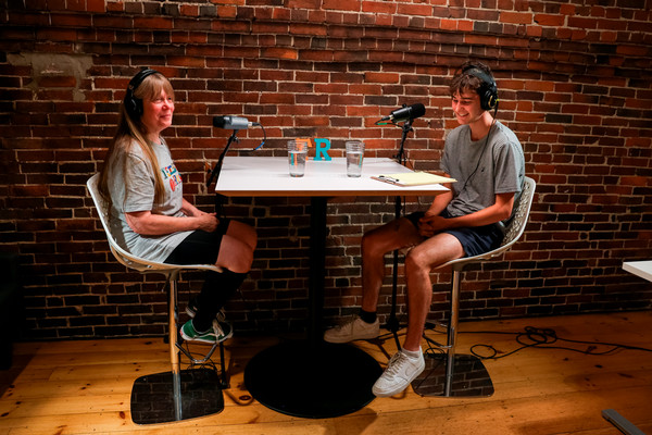 Brooks sits with another person at a table with microphones in front of them.